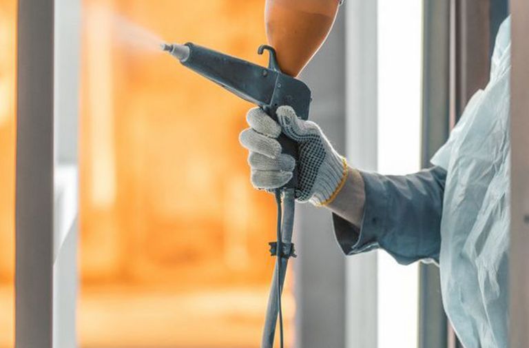 A man spraying powder coating on a hung metal substrate